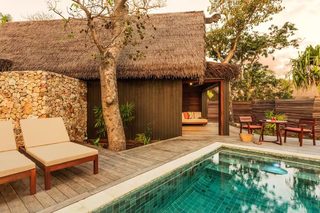 A poolside area with lounge chairs, a thatched-roof structure, and a stone wall.