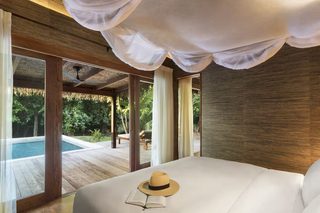 A bedroom with a large bed, a hat, and an open book on the bed. There is a view of a pool and outdoor furniture.