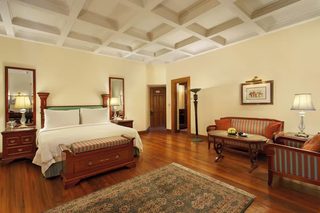 A hotel room with a large bed, wooden furniture, a patterned rug, and a ceiling with a grid design.