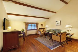 A spacious living room with a wooden floor, a sofa, a chair, a table, and a desk.