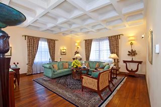 A spacious living room with a wooden floor, a green sofa set, a coffee table, and a patterned rug.
