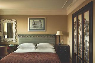 A hotel room with a bed, a nightstand, a lamp, a framed picture on the wall, and a mirror with a decorative frame.