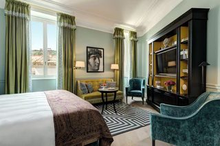 A hotel room with a bed, a sofa, a small table, a cabinet, and a chair.