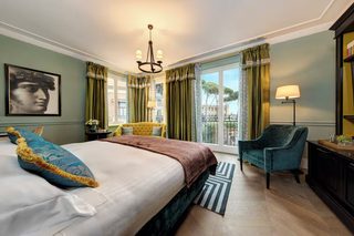 A spacious bedroom with a large bed, a chair, a desk, and a view of the outside.