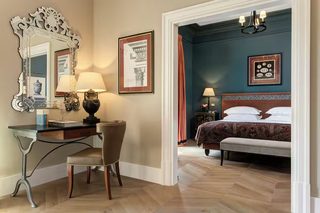 A hotel room with a desk, chair, bed, and two lamps.