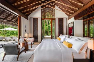 A spacious bedroom with a large bed, a sitting area with a table and chairs, and a view of lush greenery outside.