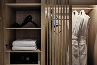 A wooden wardrobe with shelves, a hairdryer, and a folded towel.