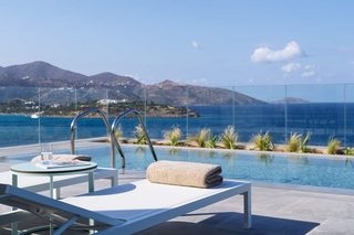 A poolside area with a lounge chair, a table with a glass of water, and a towel.