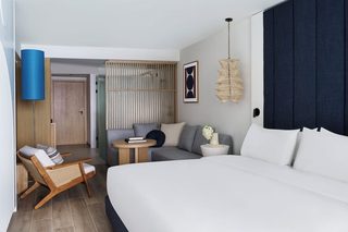 A modern hotel room with a large bed, a sofa, a small round table, a chair, and a decorative wall piece.
