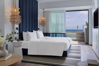 A modern hotel room with a large bed, a view of the ocean, and a balcony with a pool.