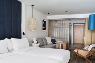 A modern hotel room with a large bed, a sofa, a small round table, and a chair.
