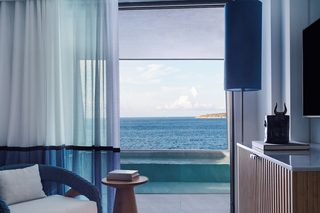 A room with a view of the sea, a sofa, a small table, and a lamp.