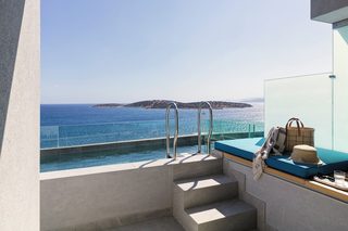 A balcony with a pool overlooking the sea, a set of stairs, and a seating area with a hat and sunglasses.