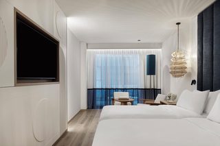 A hotel room with a large bed, a TV, a balcony with a view, and a hanging light fixture.