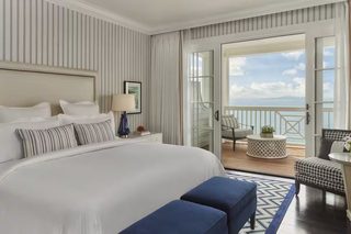 A hotel room with a large bed, a balcony with a view of the sea, a small round table, and a chair.