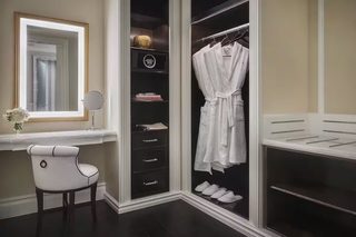 A walk-in closet with a robe hanging, a mirror, and a chair.