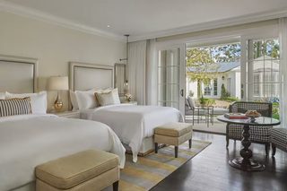 A hotel room with two beds, a dining table, and a view of the outside.