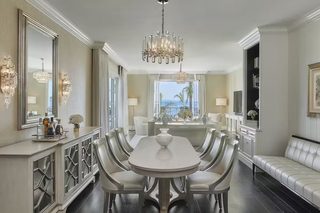 A dining area with a white table and chairs, a chandelier, and a view through a window.