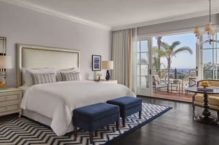 A hotel room with a large bed, a desk with a chair, and a balcony with a view of palm trees and the ocean.