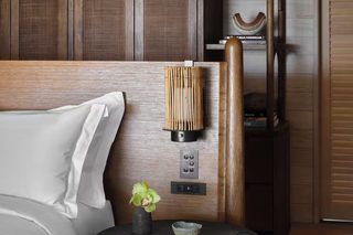 A modern bedroom with a wooden headboard, a bedside table with a vase of flowers, and a small shelf with books.
