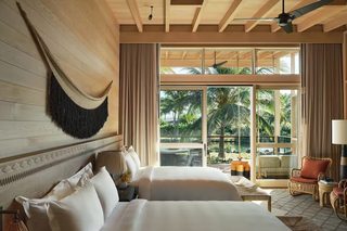 A bedroom with two beds, a hammock, and a view of a tropical garden.