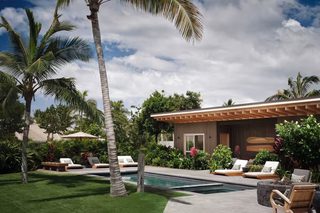 A modern poolside area with lounge chairs, a pool, and a building with a wooden pergola.