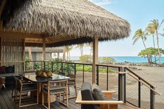 A wooden deck with a thatched roof, outdoor furniture, and a view of the ocean.