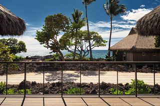 A beach view with thatched-roof huts, palm trees, and a wooden deck.