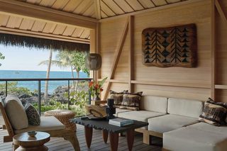 A cozy lounge area with a wooden ceiling, a sofa set, a coffee table, and a view of the ocean.